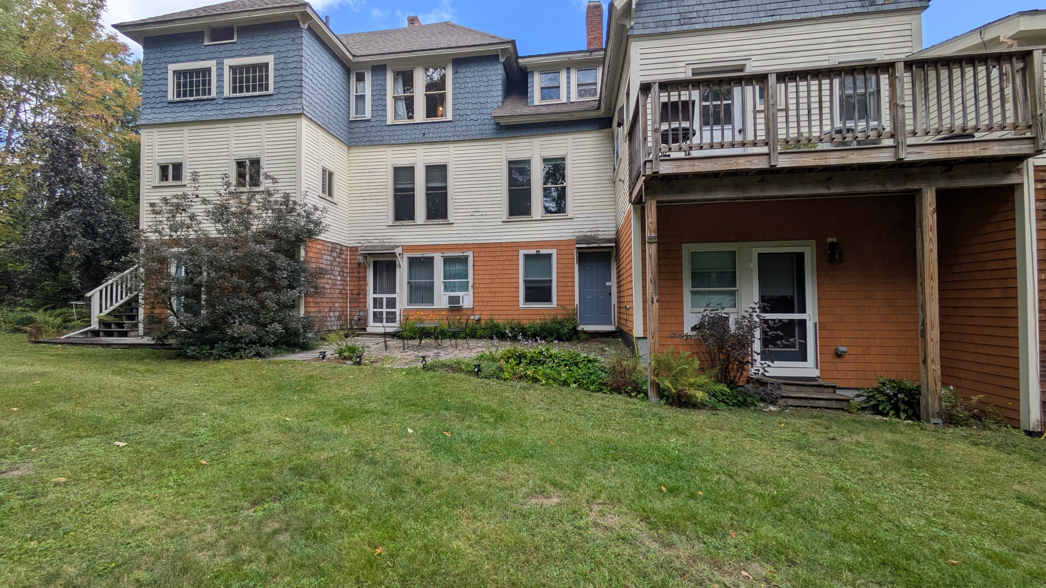 The house, with slate-blue shingles, warm-white siding, cedar tones, and a green lawn